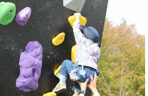 帽子をかぶった小さな子どもが大人に支えられてホールドを掴む様子